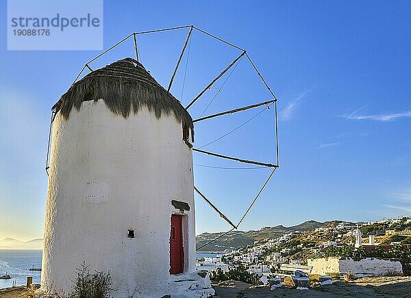 Berühmte Touristenattraktion von Mykonos  Kykladen  Griechenland. Traditionelle  weiß getünchte Windmühle auf einem Hügel mit Blick auf die Stadt Chora am Wasser. Sommer  Sonnenuntergang  blauer Himmel. Reiseziel  ikonische Aussicht