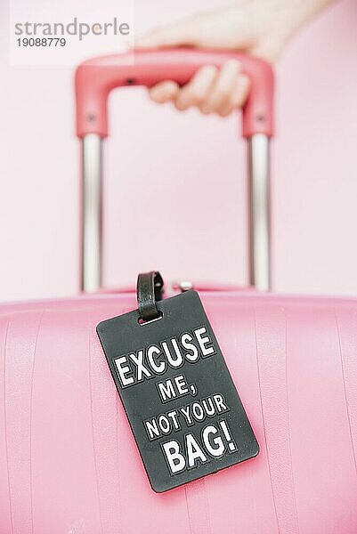 Person s Hand hält Griff Reisekoffer mit Ihrer Tasche Tag gegen rosa Hintergrund