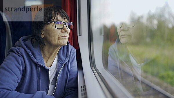 Ältere Dame mit Brille reist im Zug und schaut aus dem Fenster  das sich im Glas spiegelt