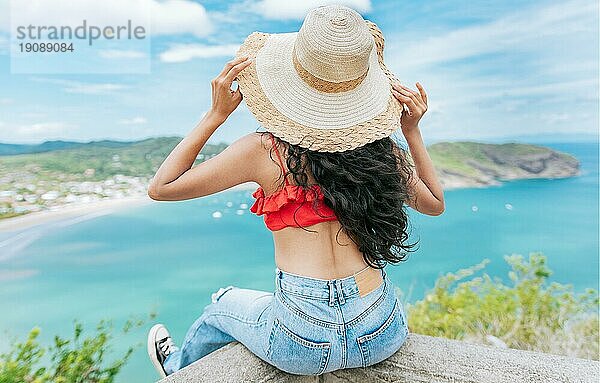 Rückansicht Tourist Mädchen sitzt an einem Aussichtspunkt mit Blick auf den Strand. Rückenansicht der Frau im Urlaub Blick auf den Strand an einem Aussichtspunkt