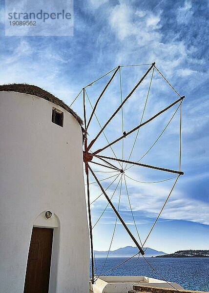 Berühmte Touristenattraktion von Mykonos  Kykladen  Griechenland. Traditionelle weiß getünchte Windmühle auf einer Anhöhe mit Blick auf den Hafen  am Meer. Sommer  Sonnenuntergang  blauer Himmel. Reiseziel  ikonische Ansicht. Vertikale Aufnahme von hinten