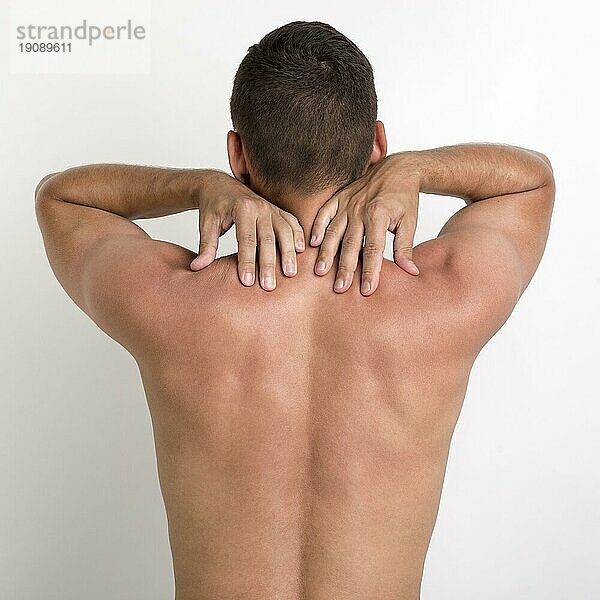 Rückansicht shirtless Mann mit Rückenschmerzen stehend gegen weiße Wand