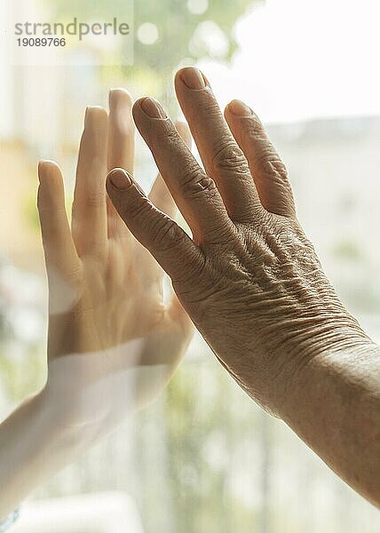 Ältere Frau  die während der Pandemie durch ein Fenster die Hand eines anderen berührt