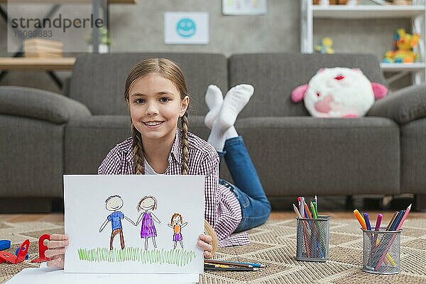 Lächelndes Mädchen liegend Teppich zeigt Zeichnung ihrer Familie gezeichnet weißes Papier