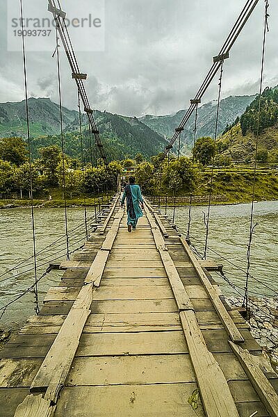 Eine Frau überquert den Fluss Indus auf einer gefährlich aussehenden Brücke in Pakistan