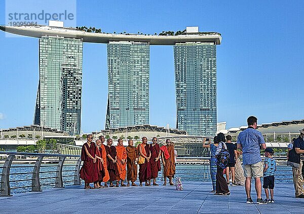 Singapur  25. Februar 2020. Asiatische buddhistische Mönche stehen für ein Gruppenfoto mit dem ikonischen Einkaufszentrum Marina Bay Sands und Shoppes im Hintergrund. Touristen warten  bis sie an der Reihe sind. Heller sonniger Tag  Asien