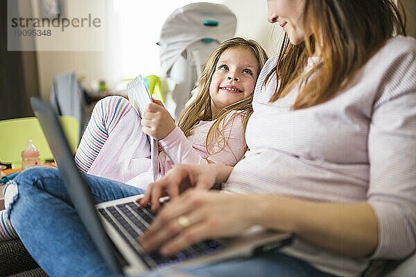 Nettes lächelndes Mädchen  das seine Mutter mit einem Laptop sucht