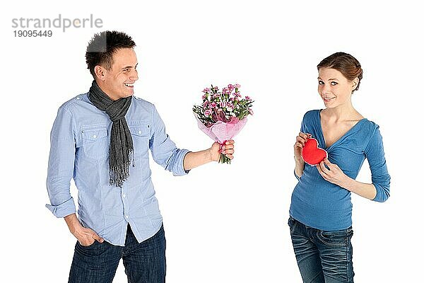 Junges attraktives glückliches Paar in Liebe. Frau gibt ihr Herz  Mann bietet Blumen  vor weißem Hintergrund