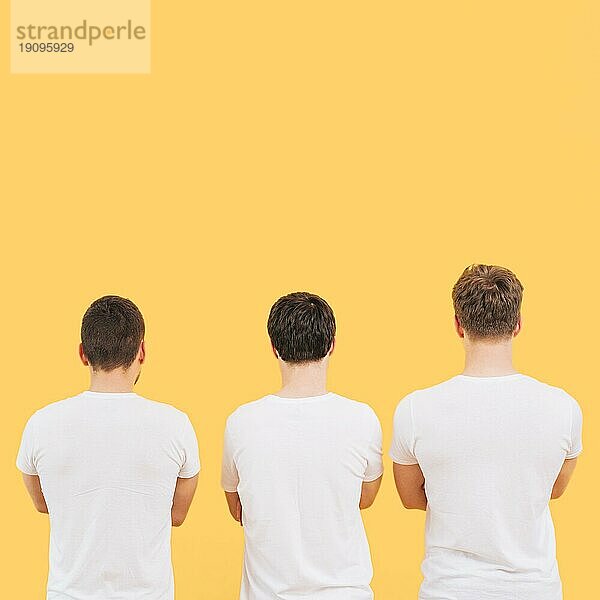 Rückansicht Männer weißes TShirt stehend gegen gelben Hintergrund