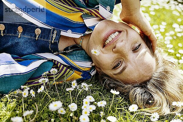 Hübsche  junge Frau liegt im Gras zwischen Gänseblümchen mit einem Gänseblümchen im Mund  Köln  Nordrhein-Westfalen  Deutschland  Wiese  gutes Wetter  Sonnenschein  fröhlich  Europa