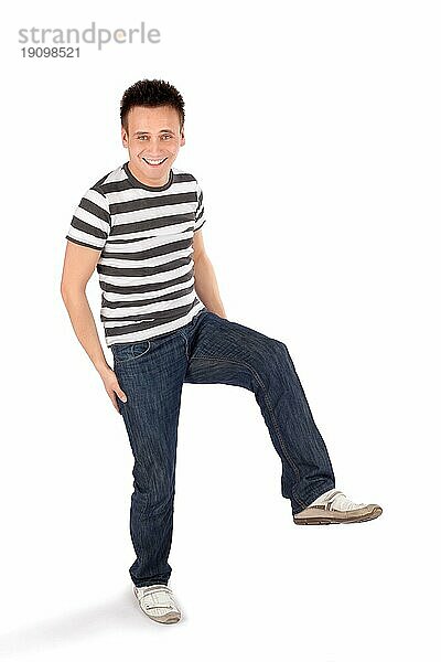 Junger fröhlicher lässiger Mann auf einem Bein stehend vor weißem Hintergrund