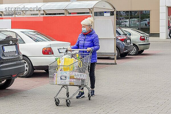 Aufnahme einer reifen Frau mit Schutzmaske und Einkaufswagen auf einem Parkplatz während einer Coronavirus Pandemie. Alltag  Kopie Raum