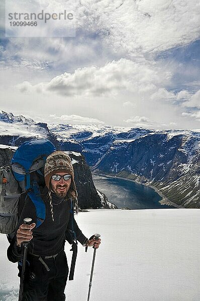 Rucksacktourist auf dem Weg zum Trolltunga Felsen mit dem Fjord im Hintergrund  Norwegen  Europa