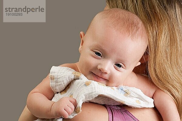 Glückliches  fröhliches  zehn Wochen altes Baby auf der Schulter der Mutter  das lächelnd in die Kamera schaut