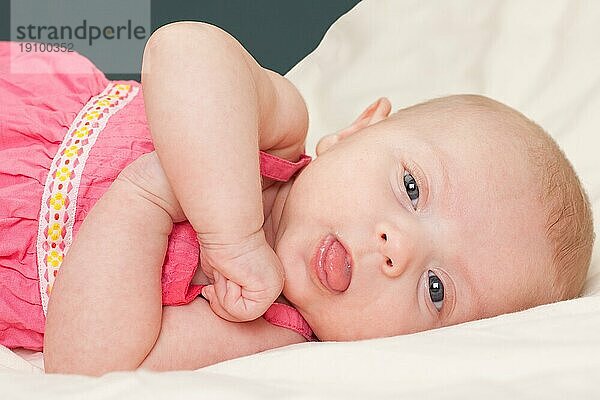 Cute Baby Mädchen Kleinkind auf dem Bett Blick in die Kamera zeigt ihre Zunge