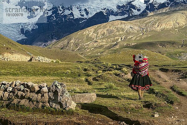 Eine peruanische Frau geht mit einem Kind auf dem Rücken in den südamerikanischen Anden spazieren