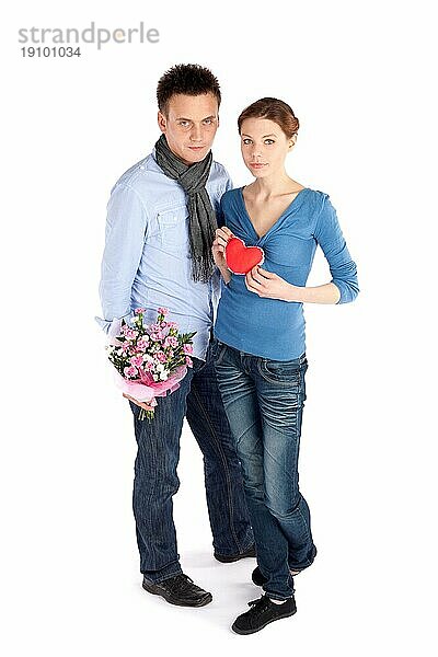 Junges attraktives Paar in Liebe. Frau hält rotes Herz  Mann hält Blumen  vor weißem Hintergrund