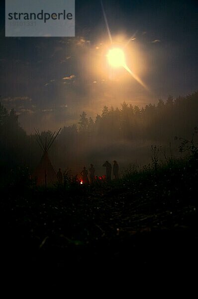 Gruppe steht um ein Lagerfeuer in mystischer Dunkelheit  die vom Mondlicht erhellt wird
