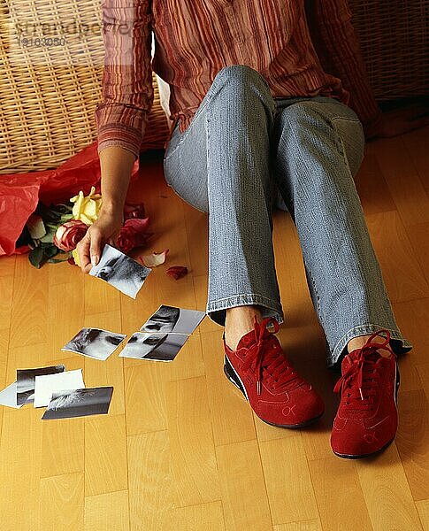 Dame sitzt auf dem Boden und puzzlet zerissenes Foto zusammen  nur Beine und Hände Digitalaufnahme