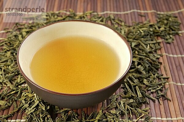 Gebrühter grüner Tee in Teeschale auf Bambusmatte. Green tea in a cup