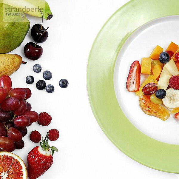 Obstsalat frisch zubereitet auf einem Teller  daneben frische ganze Früchte