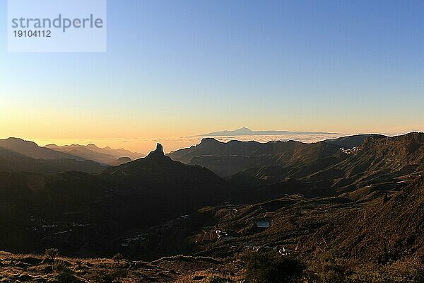 Blick auf den Roque Nublo auf Gran Canaria mit der Silhouette des Berges Teide im Hintergrund und einer Meereswolke. Sonnenuntergang auf Gran Canaria. Roque Nublo und El Teide zusammen