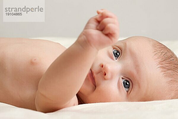 Zehn Wochen alt niedlichen kleinen Baby Mädchen Kleinkind mit neugierigen Blick auf ihr Gesicht liegen bequem auf dem Bett
