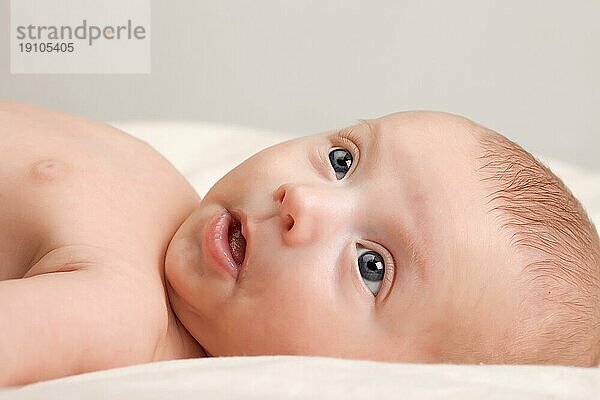 Zehn Wochen alt niedlichen kleinen Baby Mädchen mit neugierigen Blick auf ihr Gesicht liegen bequem auf dem Bett