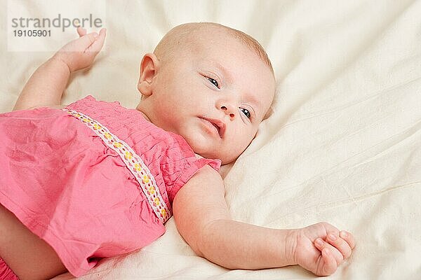Baby Mädchen Kleinkind trägt rosa Kleid liegend bequem auf dem Bett