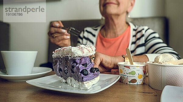 In einem Cafe. Bunter Kuchen  Eiscreme und Kaffee auf dem Tisch. Hand einer älteren Frau mit einer Kuchengabel. Kopierraum
