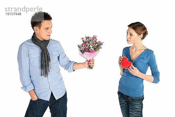 Junges attraktives Paar in Liebe. Frau gibt ihr Herz  Mann bietet Blumen  vor weißem Hintergrund
