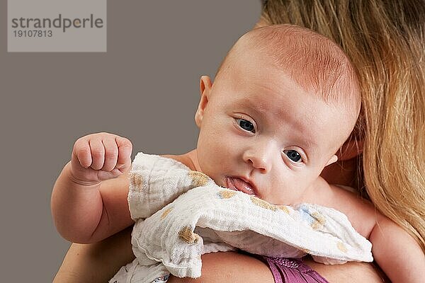 Kleines süßes zehn Wochen altes Baby auf der Schulter der Mutter  das in die Kamera schaut