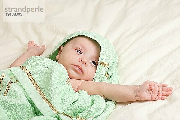 Zehn Wochen alt niedlichen kleinen Baby Mädchen Kleinkind in Handtuch gewickelt Stretching ihre Arme auf dem Bett liegend