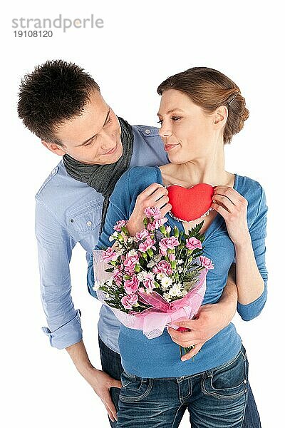 Junges  verliebtes Paar. Frau hält rotes Herz  Mann hält Blumen  vor weißem Hintergrund