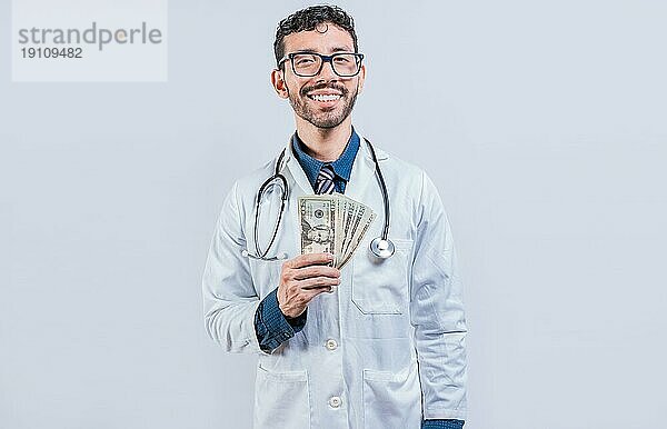 Glücklicher junger Arzt hält Geld isoliert. Hübscher Arzt zeigt Geld auf weißem Hintergrund