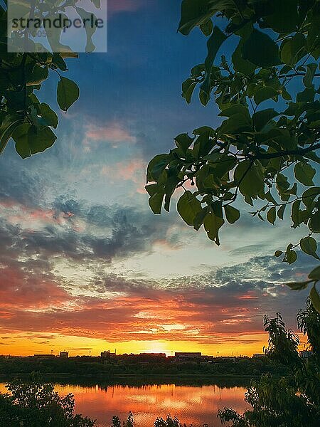 Gorgeous Sommer Sonnenuntergang aus dem Garten unter den grünen Bäumen gesehen. Sonnenuntergang Blick über die Stadt Horizont reflektiert auf dem ruhigen Delia See Wasser in Ungheni Stadt  Moldawien  Europa