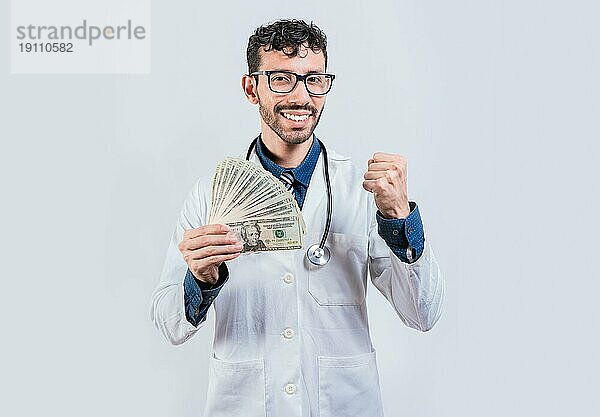 Lächelnder junger Arzt hält Geld isoliert. Fröhlich Arzt hält Dollar Rechnungen isoliert