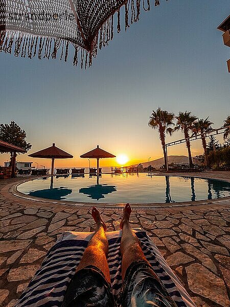 Füße eines Mannes in einem Pool  der einen Sonnenuntergang im Sommerurlaub genießt