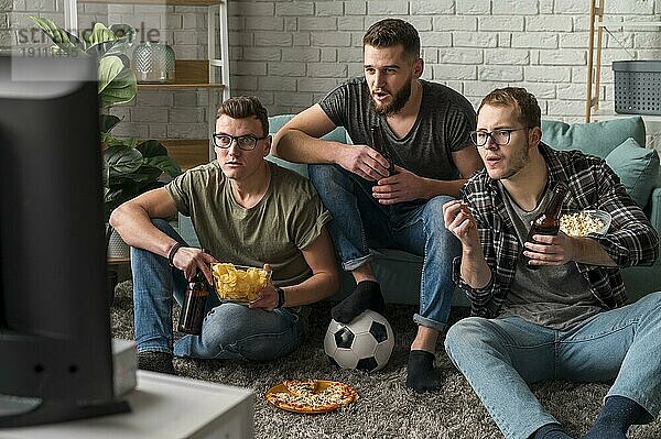 Frontansicht drei männliche Freunde beobachten Sport TV zusammen  während mit Snacks Bier