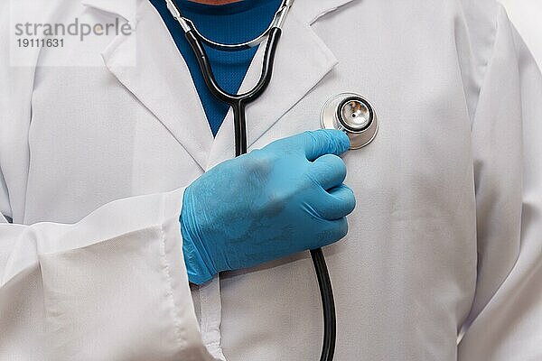 Nahaufnahme eines Arztes mit blauen Latexhandschuhen und einem Stethoskop in der Hand  der sich selbst auskultiert