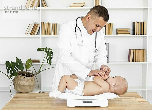 Lächelnder Arzt wiegt kleines Baby