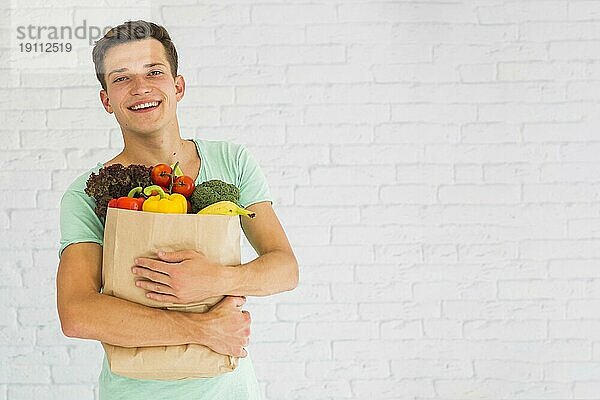 Lächelnder junger Mann hält frisches Gemüse Früchte Lebensmittelgeschäft Papiertüte