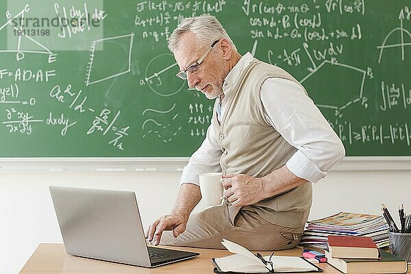 Senior Professor sitzt am Schreibtisch und tippt auf einem Laptop