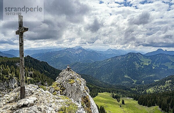 Bergsteigerin sitzt am Gipfel des Taubenstein mit Gipfelkreuz  Mangfallgebirge  Bayern  Deutschland  Europa