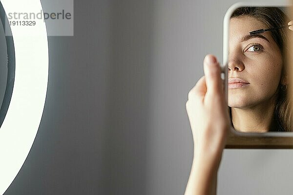 Frau bürstet ihre Augenbrauen  während sie nach der Behandlung mit Kopierraum in den Spiegel schaut