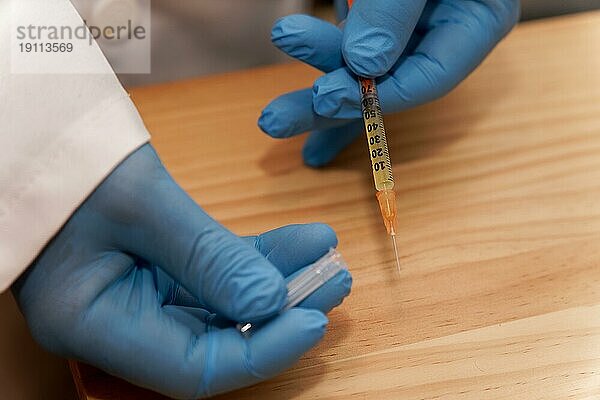 Hände eines Arztes in blauen Latexhandschuhen mit einer Spritze in der Hand auf dem Tisch in seinem Büro