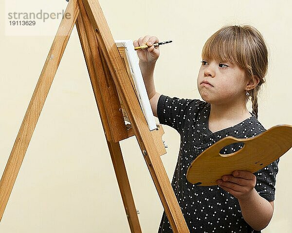 Seitenansicht Mädchen mit Down Syndrom malt mit Staffelei