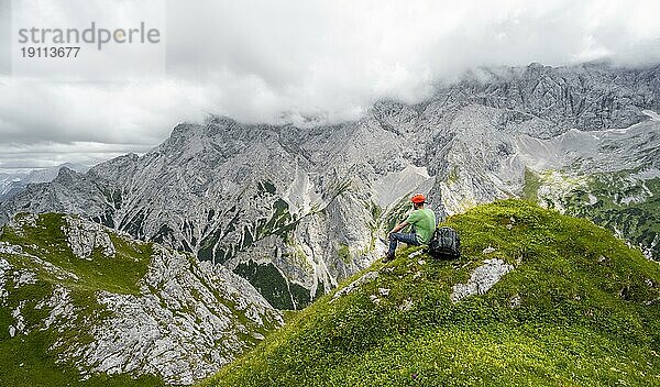 Bergsteiger rastet und genießt die Aussicht  auf dem Schafsteig am Waxensteinkamm  Ausblick auf wolkenverhangene felsige Berglandschaft mit Jubiläumsgrat  Wettersteingebirge  Garmisch-Partenkirchen  Werdenfelser Land  Oberbayern  Bayern  Deutschland  Europa