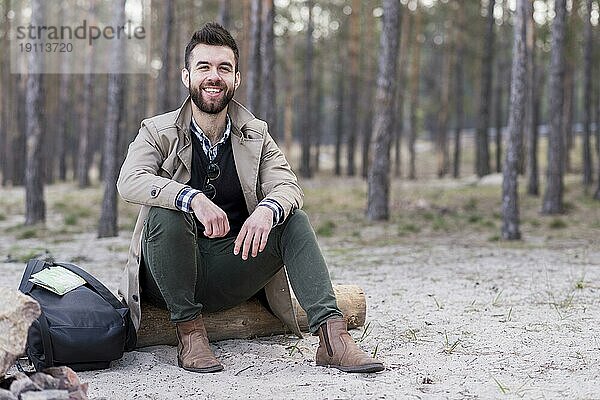 Porträt lächelnd männlichen Reisenden sitzen Strand mit seinem Rucksack