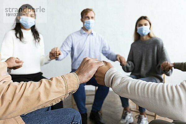 Menschen mit medizinischen Masken halten sich an den Händen Gruppentherapiesitzung